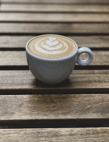 Close-up of a frothy cappuccino with latte art served on a rustic wooden tray.