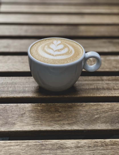 Close-up of a steaming cup of cappuccino with intricate latte art on a wooden table.