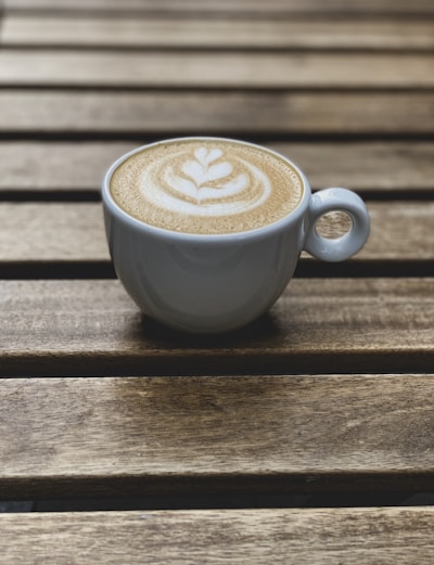 A close-up of a steaming cappuccino with latte art on a rustic wooden table.