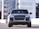 A silver luxury SUV is parked in an urban setting with modern buildings in the background. The vehicle has a sleek and polished exterior with prominent headlights and a distinctive front grille.