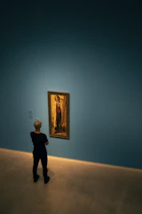 A close-up photo of a person inspecting a luminous painting in a modern gallery setting.