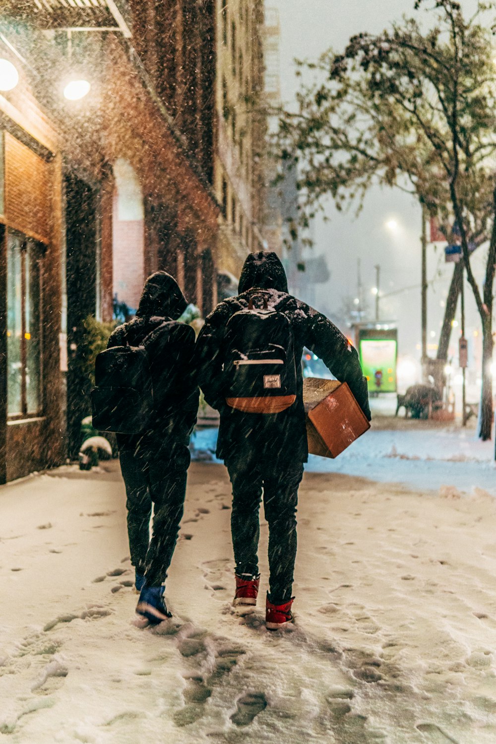 two people walking beside brown concrete building during snow