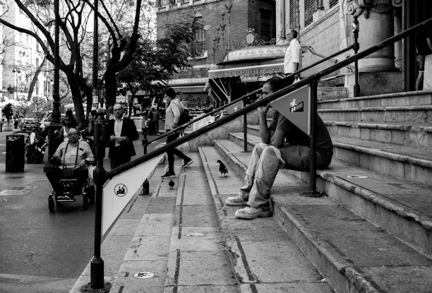 Black and white illustration of Quinho character interacting with diverse people using accessibility tools.