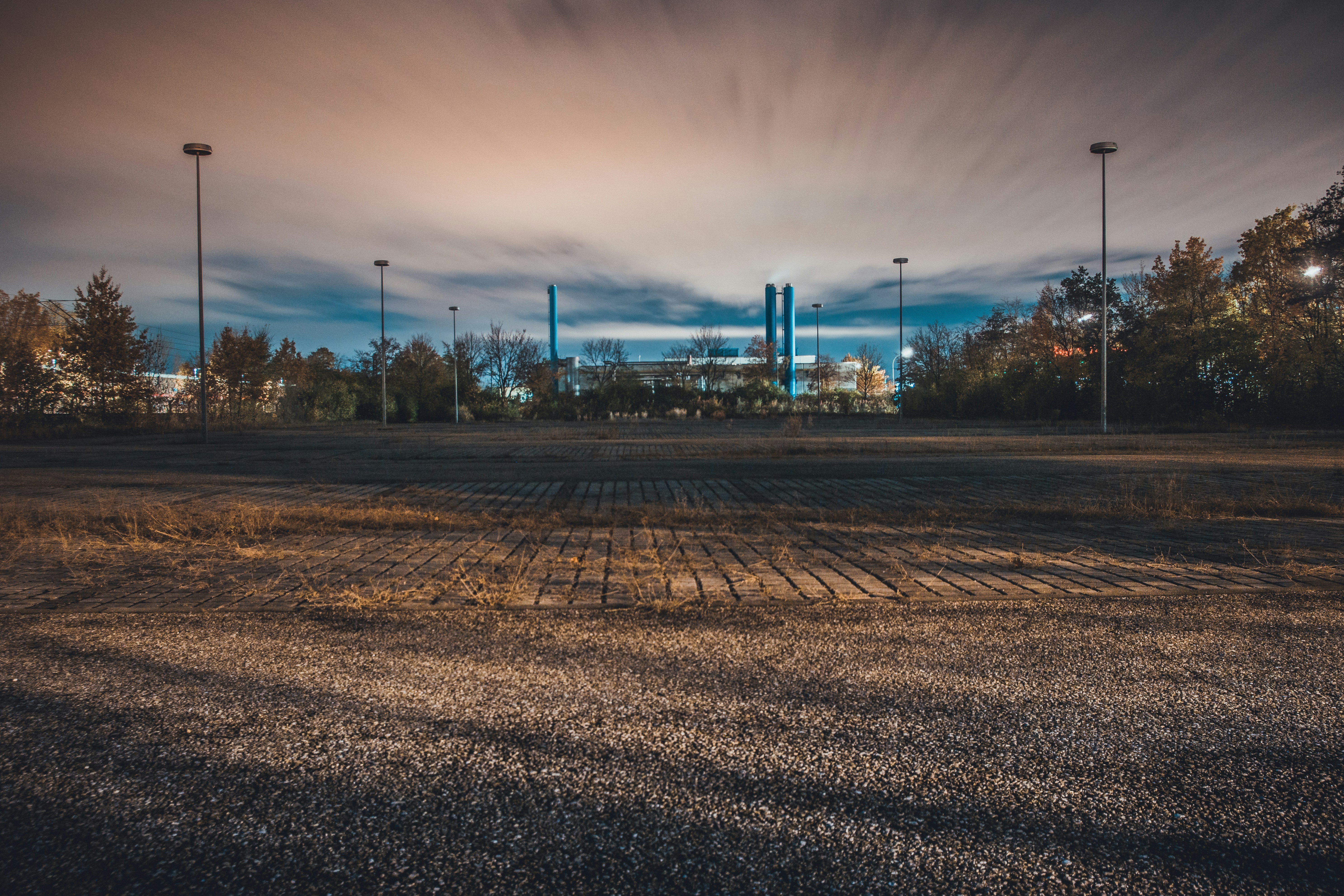 Dark industrial chemical plant at night, cool blue lighting, heavy machinery silhouettes