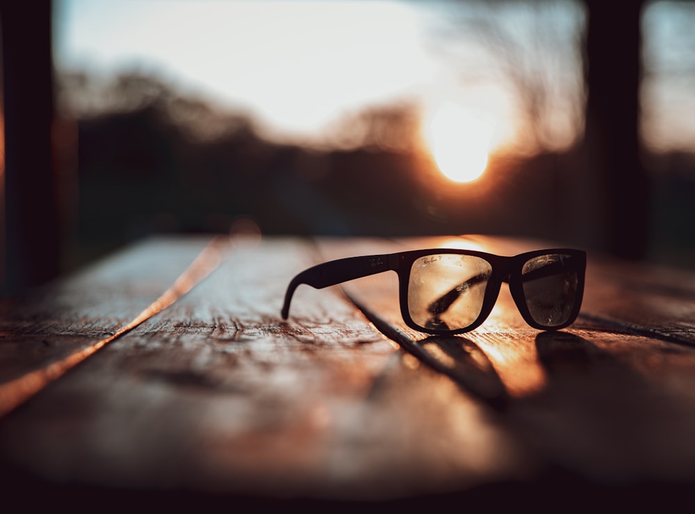 selective focus photography of black sunglasses on brown surface