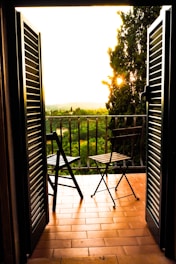 Private balcony of the suite featuring comfortable chairs and a small table, framed by pink and orange sky at sunset.