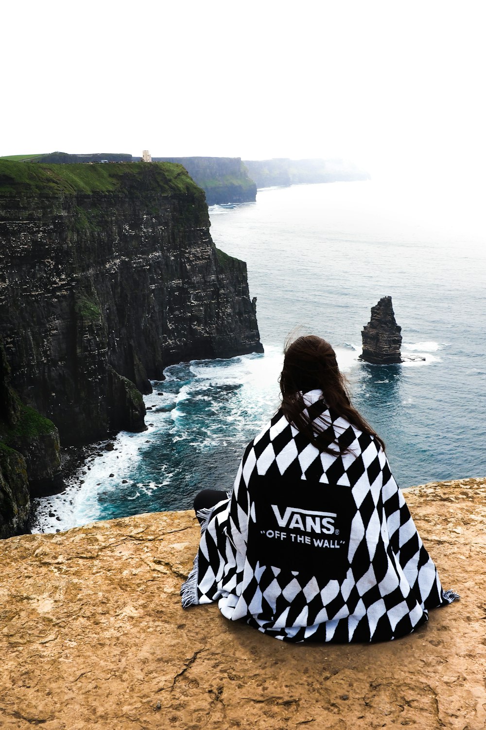 person sitting on beach cliff viewing body of water during daytime