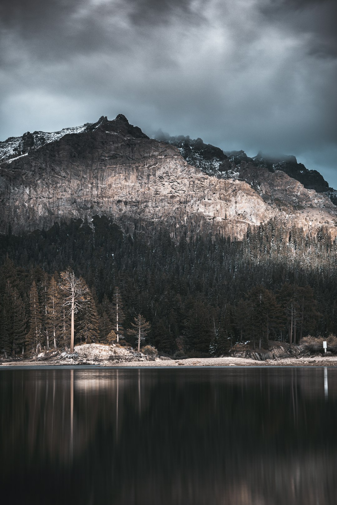 lake by mountain under gray skies at daytime