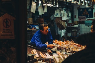 A friendly fishmonger handing fresh seafood to a smiling customer at a coastal market stall.