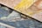 Close-up view of two textured, overlapping canvases displaying vibrant brushstrokes. One canvas features swirling patterns of yellow and beige, while the other showcases a mix of blue and orange tones. The detailed texture of the canvas is visible, highlighting the artistic style.