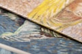 Close-up view of two textured, overlapping canvases displaying vibrant brushstrokes. One canvas features swirling patterns of yellow and beige, while the other showcases a mix of blue and orange tones. The detailed texture of the canvas is visible, highlighting the artistic style.