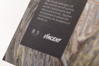 A textured, tilted display of artistic text set on a dark background, featuring a mix of English and Chinese characters. The backdrop appears to be part of a larger artwork, possibly a painting, with visible textured brushstrokes.