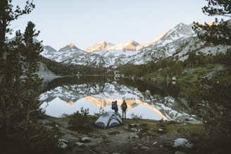 A hiker setting up a compact, waterproof tent beside a serene mountain lake at sunrise.