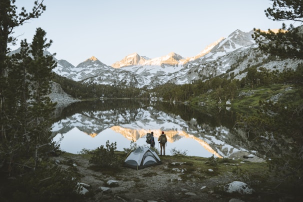 A hiker setting up a compact, waterproof tent beside a serene mountain lake at sunrise.