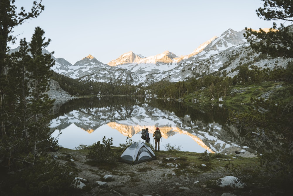 two people standing next to a tent near a lake