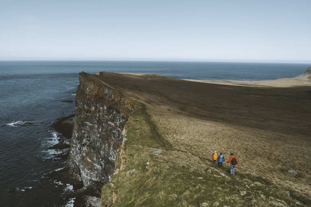 people trekking on cliff facing ocean