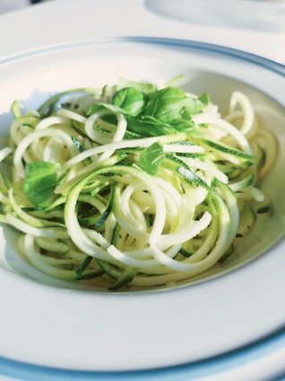 A plate of zucchini noodles garnished with fresh basil leaves, served in a white bowl with a blue rim.