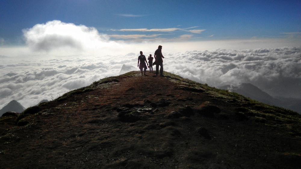 three person on mountain peak with sea of clouds