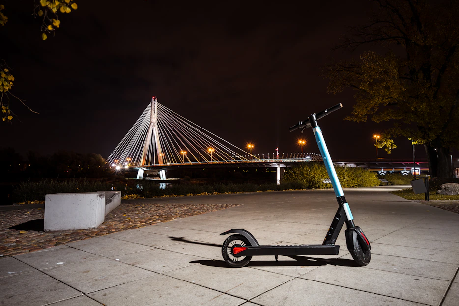 A sleek Sutton electric scooter parked on a city street at sunset