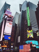 Skyscrapers dominate the urban skyline, adorned with vibrant and large electronic billboards displaying advertisements and brand names. An American flag is prominently displayed in lights.