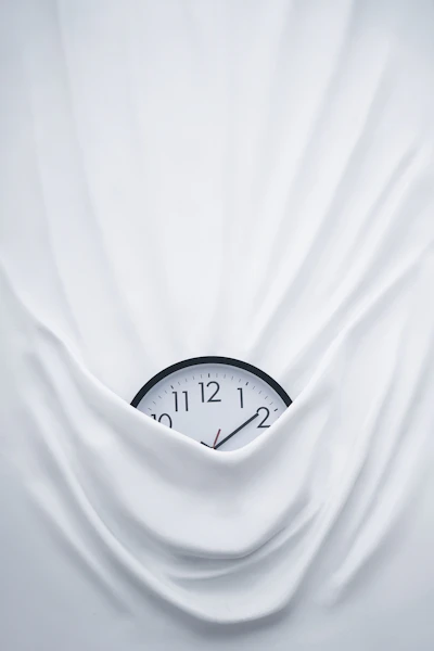 A round black analog clock photographed close-up on a linen surface