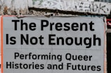 A poster with bold black text on a pale background, titled 'The Present Is Not Enough', followed by 'Performing Queer Histories and Futures'. The poster is partially torn and pasted on a textured wall with graffiti.