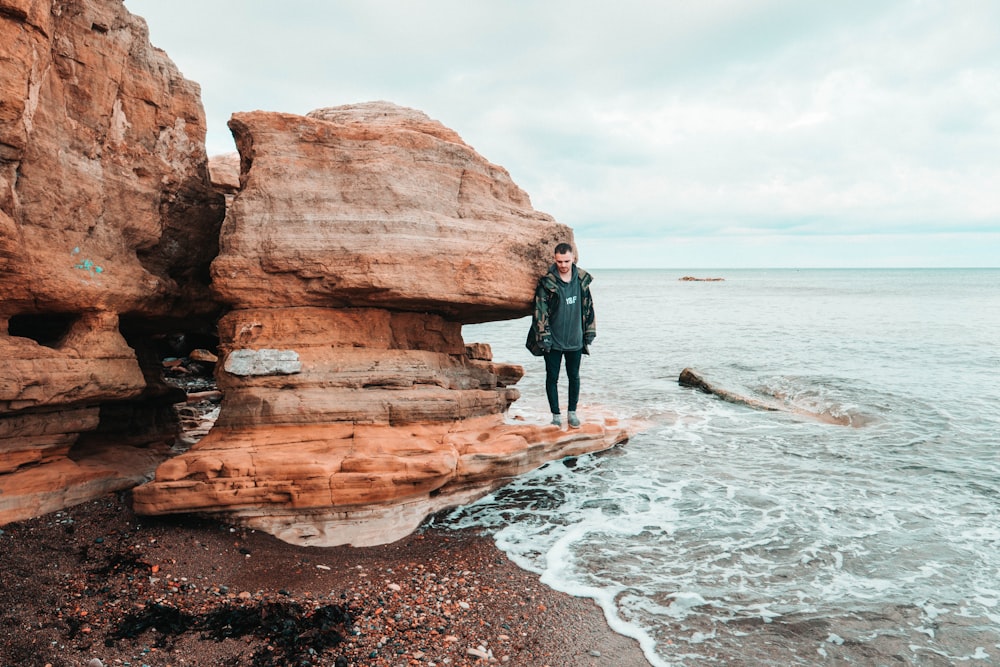 man standing on brown rock beside beach
