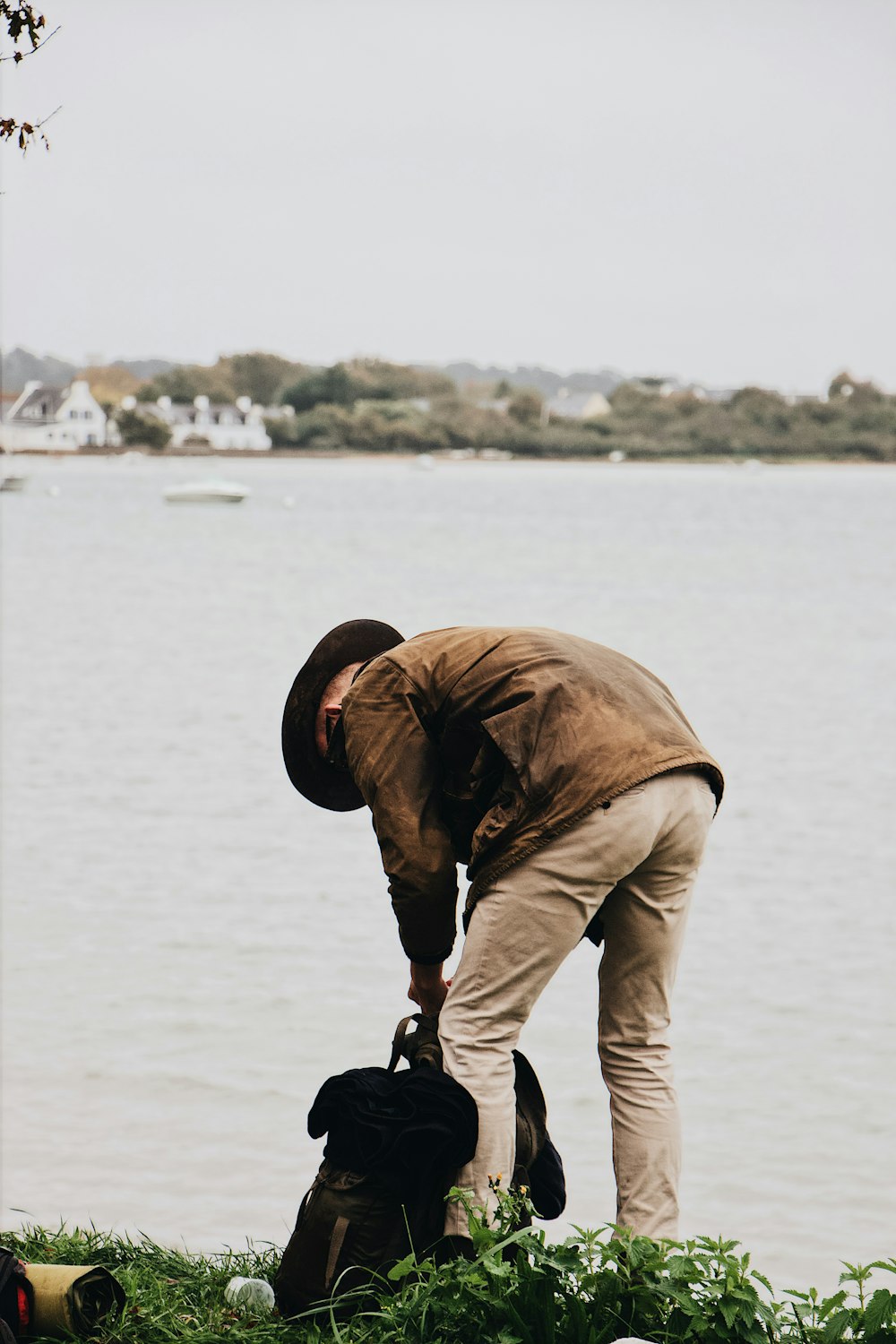 man picking up backpack near body of water