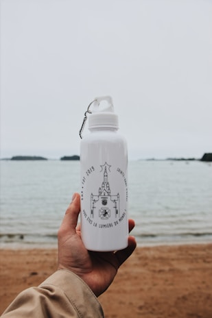 A stainless steel water bottle engraved with a sacred heart design, resting on a wooden table.