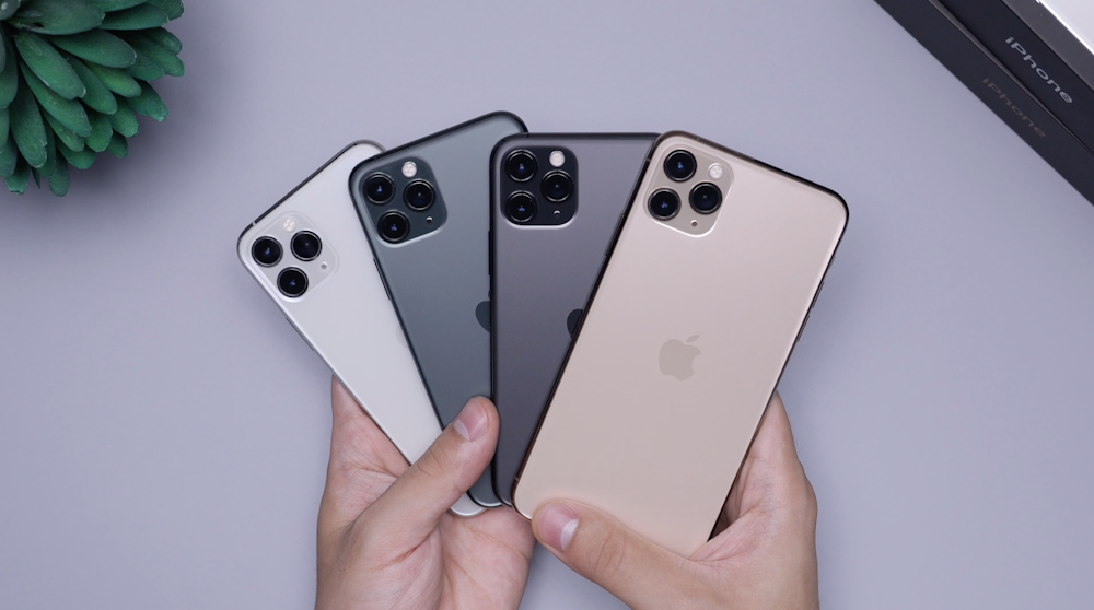 two space gray and two silver iPhone 11's fanned out being held in two hands over a grey desk