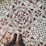 Intricate patterned floor tiles feature ornate white designs on a brown background, including floral and heraldic motifs with Latin script encircling the patterns. A pair of brown leather shoes stand on the tiles, partially visible in the image.