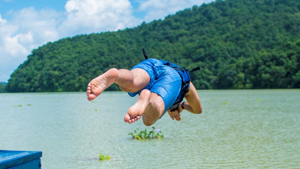 man about to dive on green body of water viewing mountain under white and blue sky during daytime