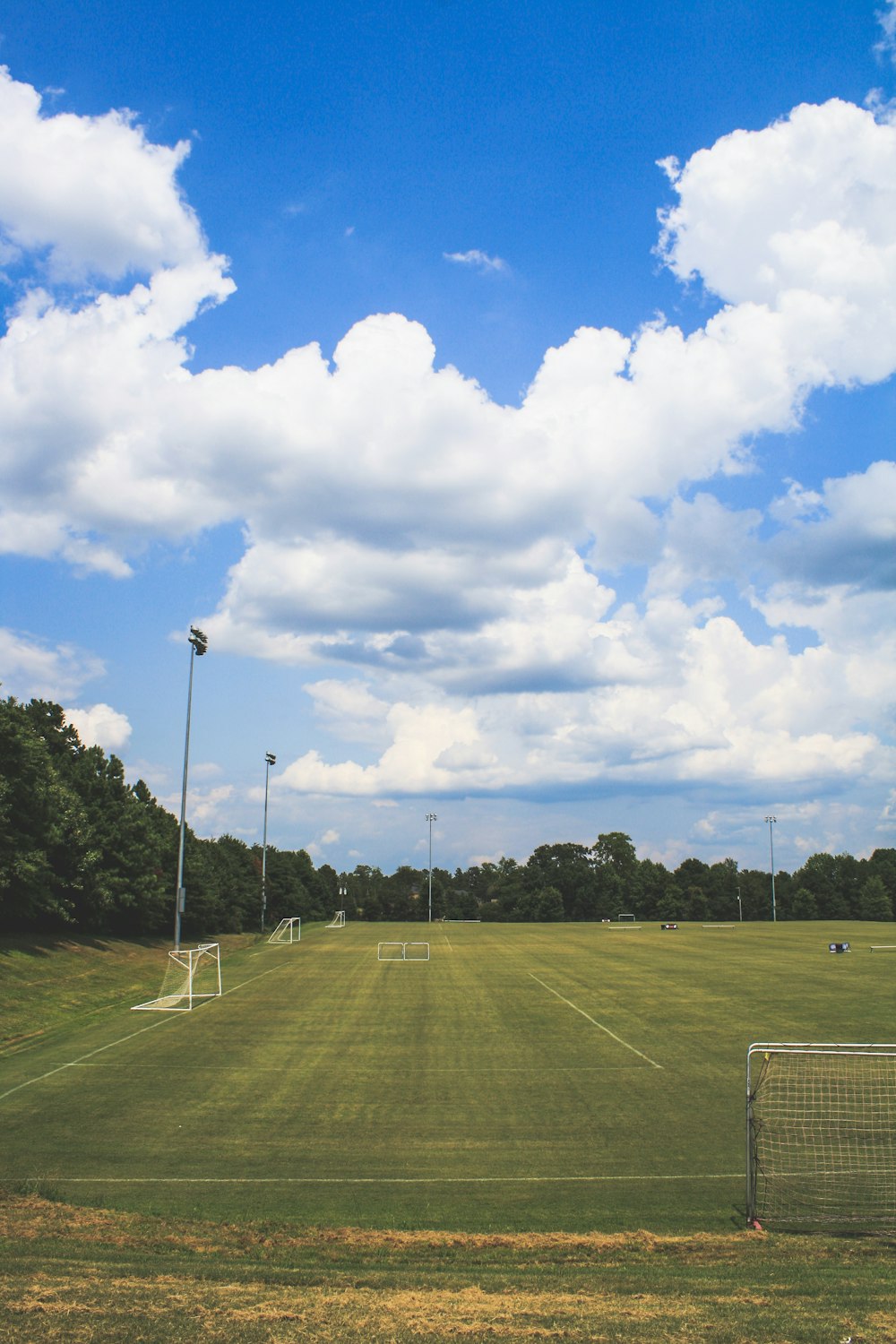 green soccer field surrounded with tall and green trees under white and blue sky during daytime