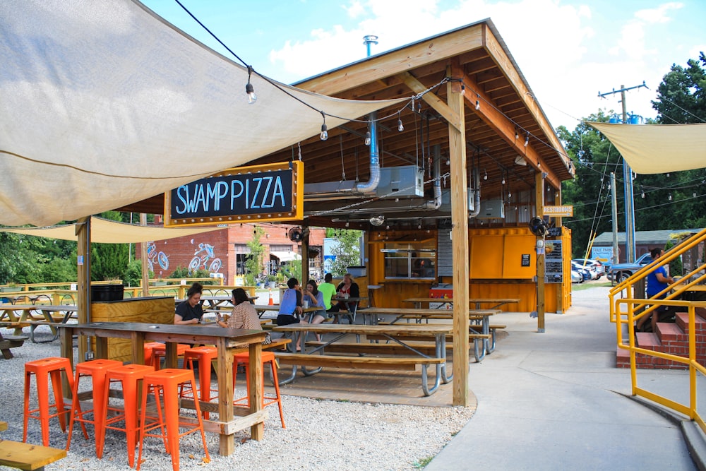 pessoas sentadas e comendo pizza em Swamp Pizza sob o céu branco e azul durante o dia