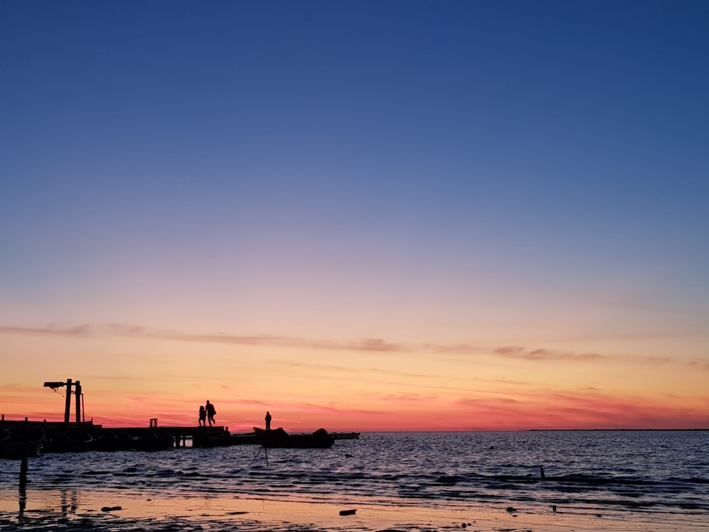 silhouette of persons on dock during golden hour