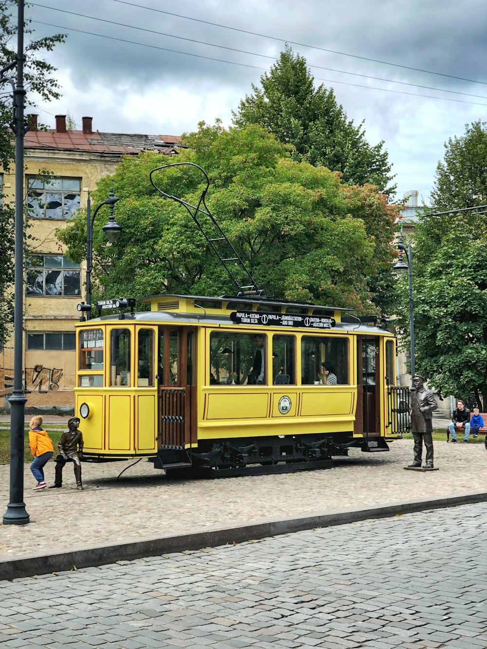 昼間の黄色い路面電車の脇に3つの像
