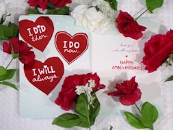 Happy Anniversary card featuring 3 red hearts with loving messages and red rose on white surface