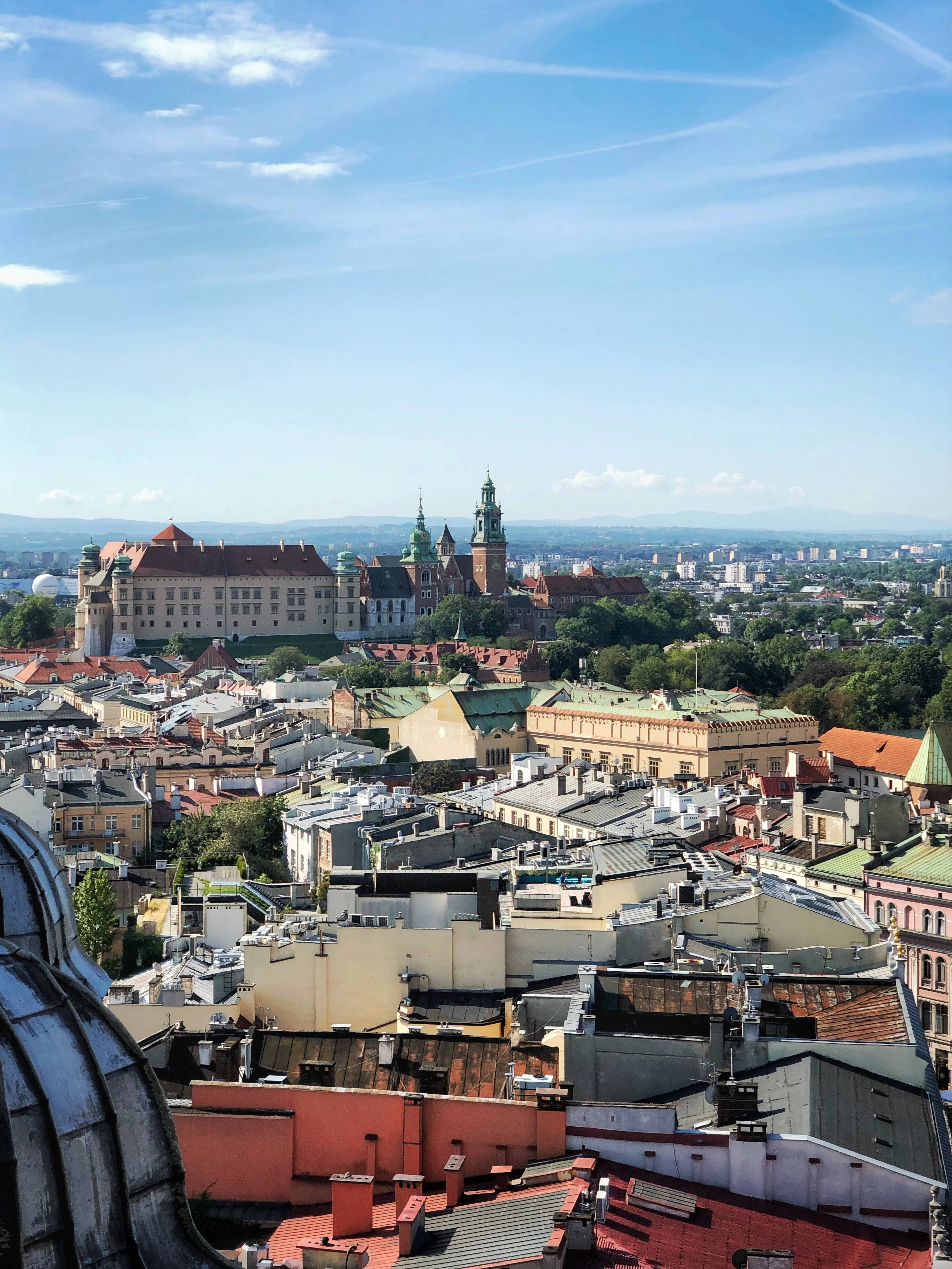 Rooftop view over Kraków's old town with Wawel Castle in the distance on a clear day.