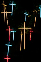 Neon crosses in various colors are arranged against a dark background, creating a glowing and mysterious atmosphere.