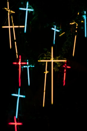 Neon crosses in various colors are arranged against a dark background, creating a glowing and mysterious atmosphere.