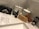 A collection of grooming products is arranged on a marble countertop. Items include a black box with grooming scissors, a tin labeled 'Beard Balm,' a bottle labeled 'Beard Oil,' a wooden brush, and a wooden comb. Decorative ceramic jars with intricate patterns stand in the background.