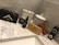 A collection of grooming products is arranged on a marble countertop. Items include a black box with grooming scissors, a tin labeled 'Beard Balm,' a bottle labeled 'Beard Oil,' a wooden brush, and a wooden comb. Decorative ceramic jars with intricate patterns stand in the background.