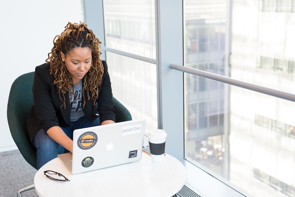 woman sits on padded chair while using MacBook during daytime