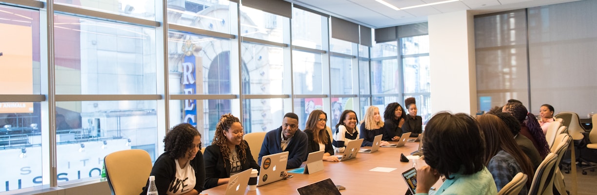 group of people sitting beside rectangular wooden table with laptops