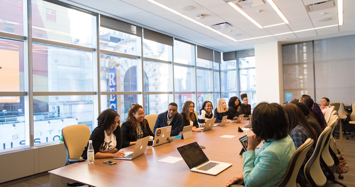 group of people sitting beside rectangular wooden table with laptops