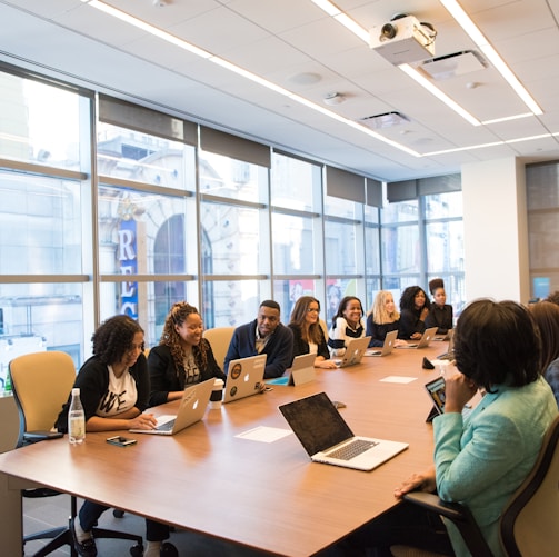 group of people sitting beside rectangular wooden table with laptops