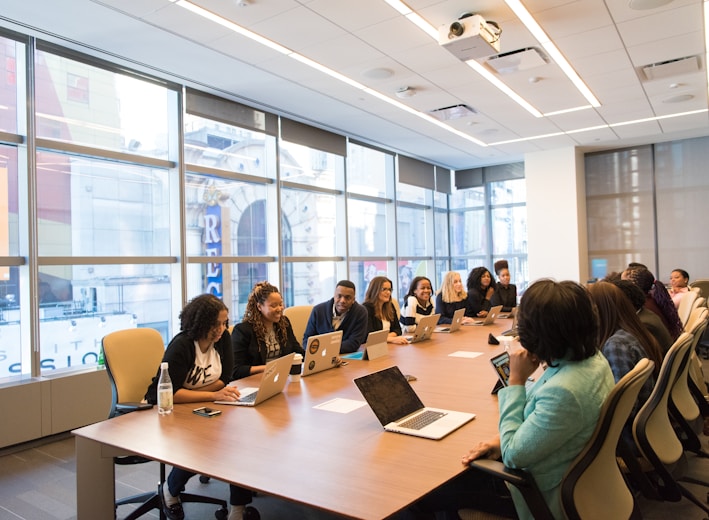 group of people sitting beside rectangular wooden table with laptops