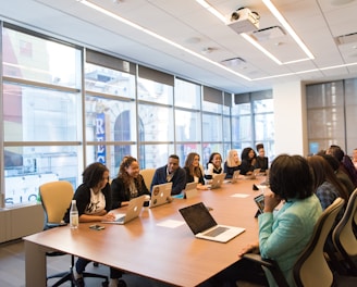 group of people sitting beside rectangular wooden table with laptops