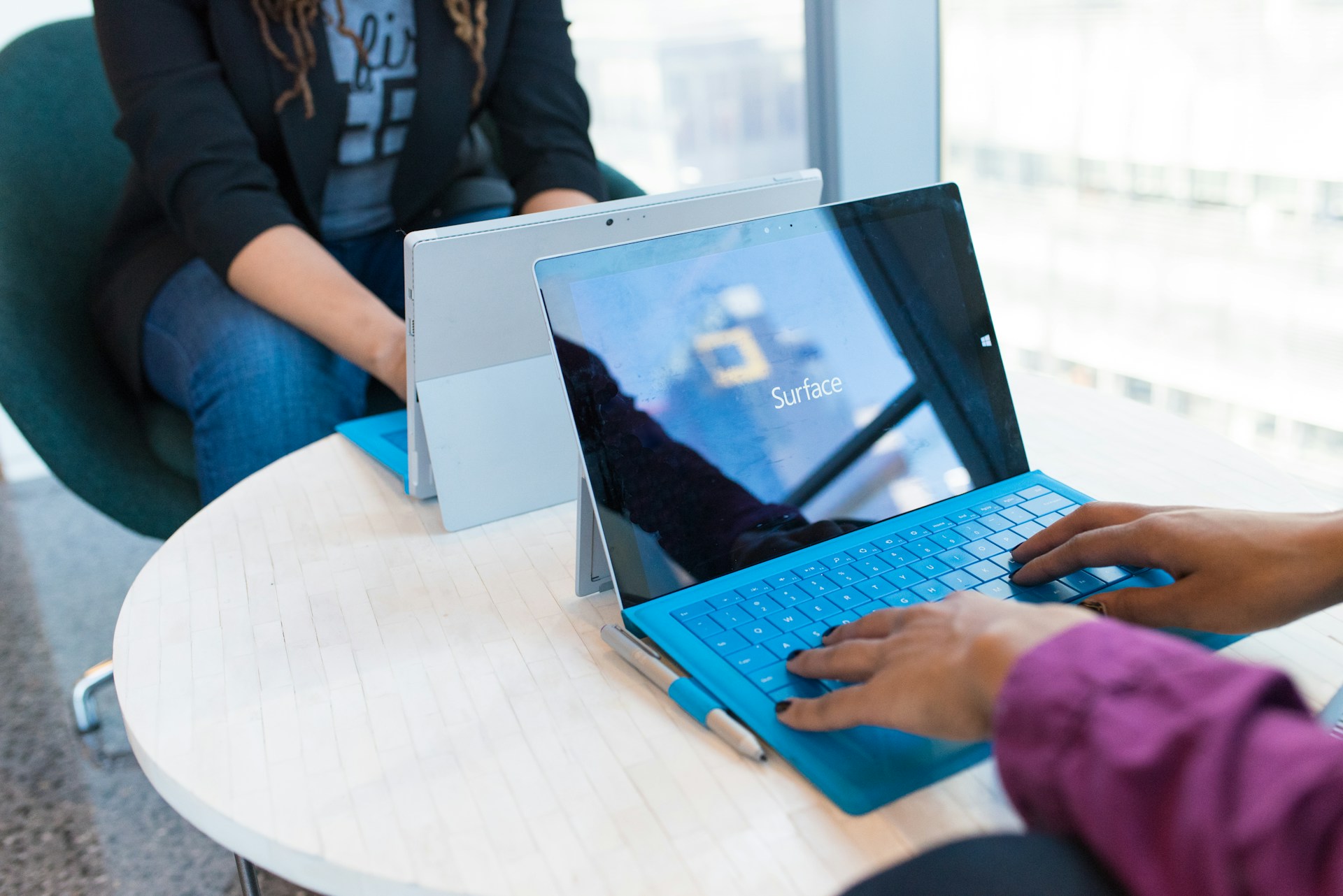 two person using laptop computers beside glass window