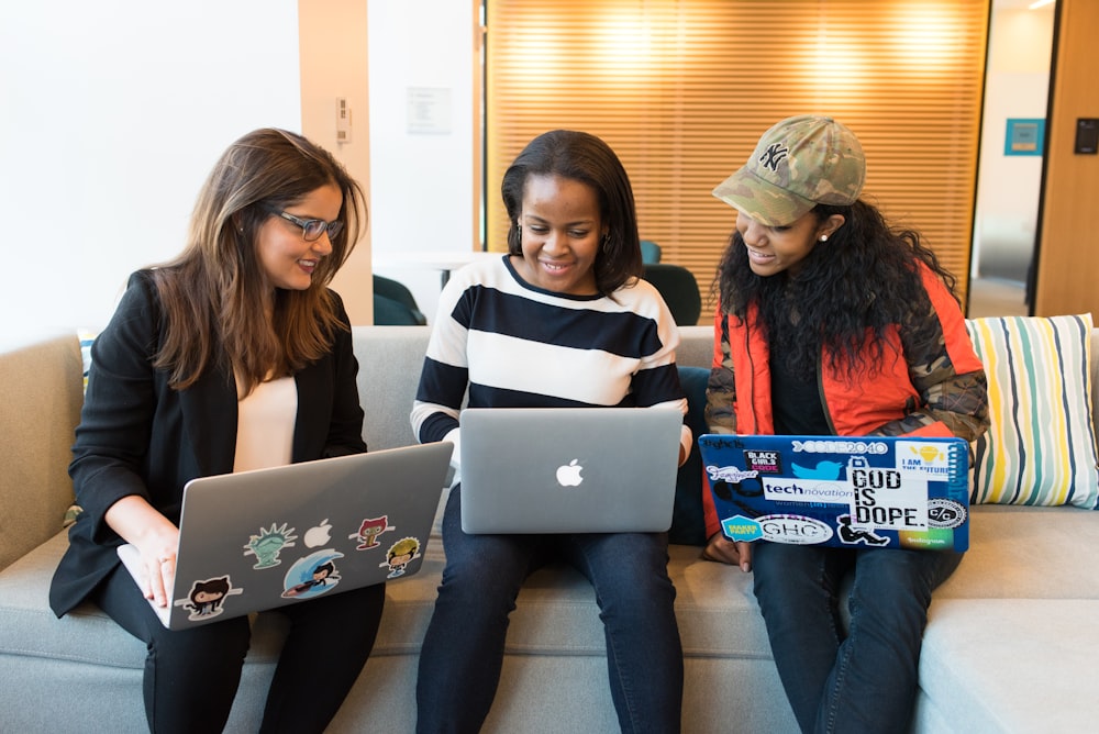 tres mujeres sentadas en el sofá con MacBook